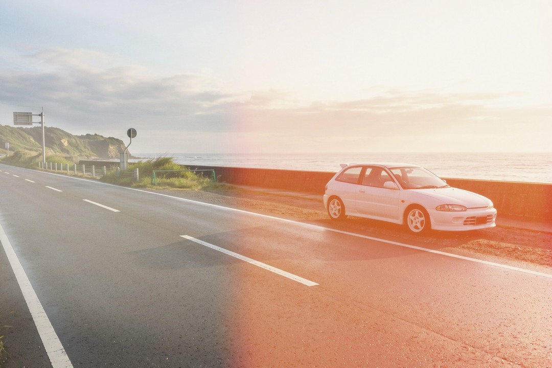 A coastal road with a white hatchback parked on the far side, and a hard orange band burning across the right half of the frame. A band like that is drawn after the colour, not by it.